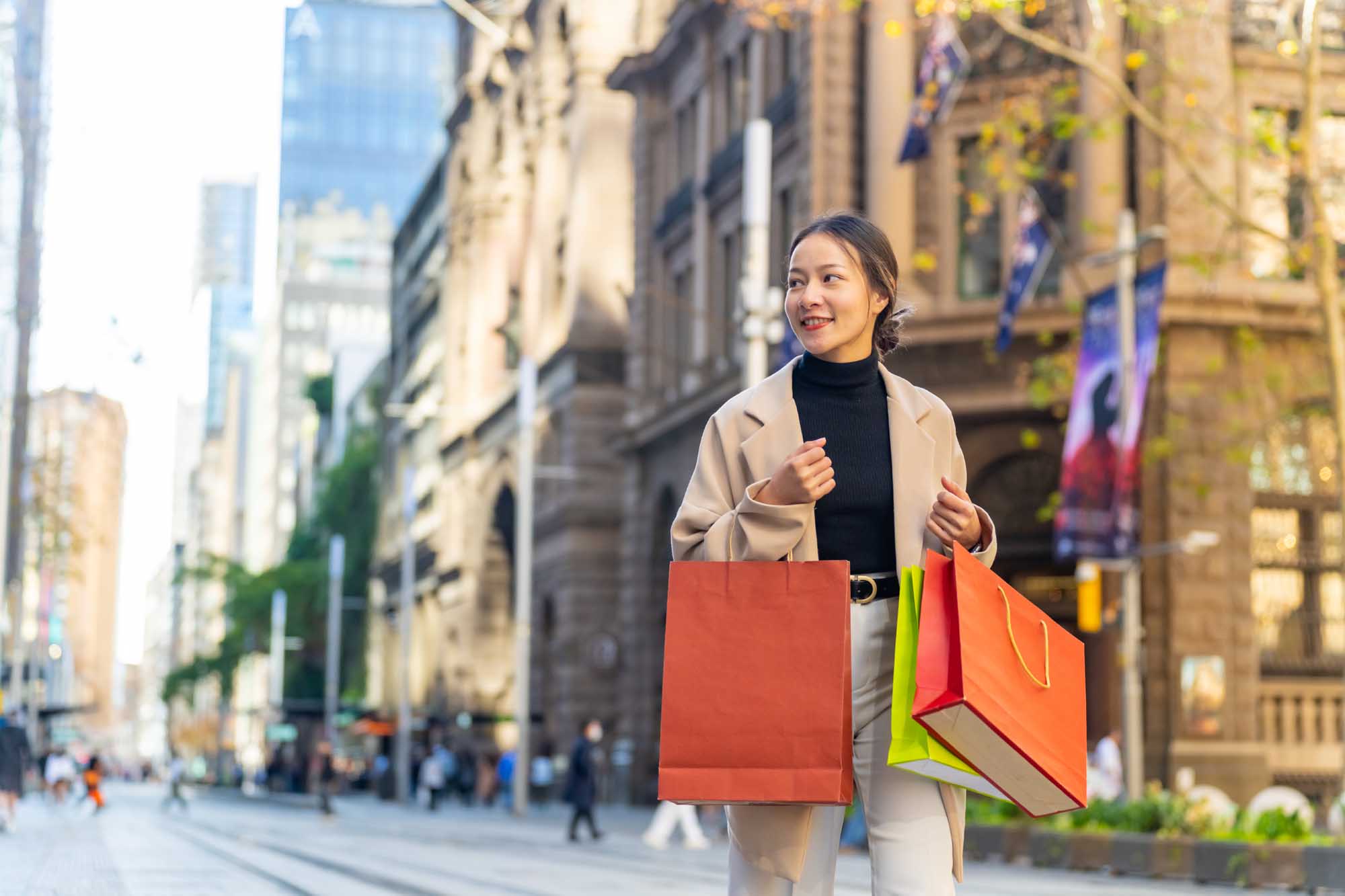 Urban Shopping in Modern City Street A stylish Asian woman carries colorful shopping bags while walking through a vibrant city street