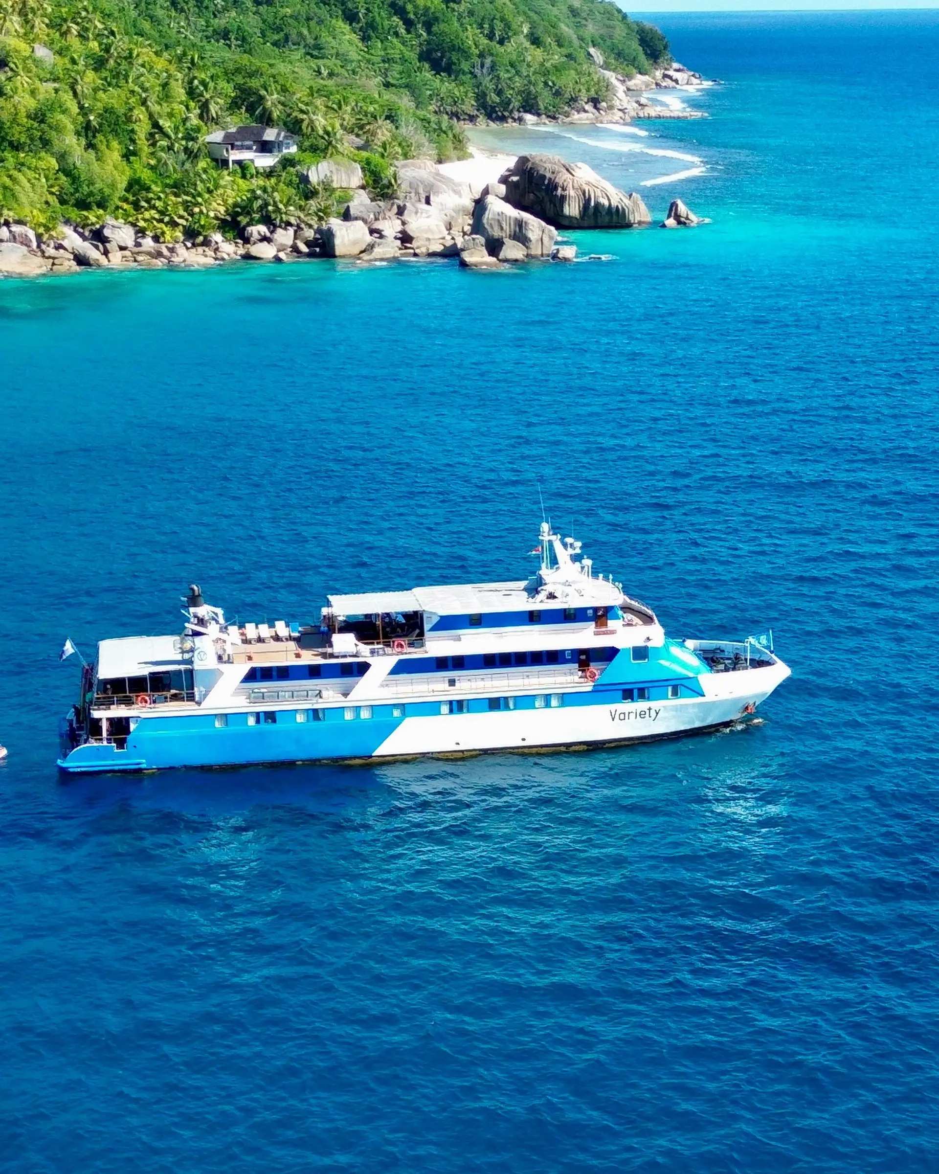 A modern cruise vessel named Variety anchors in crystal-clear turquoise waters off a pristine