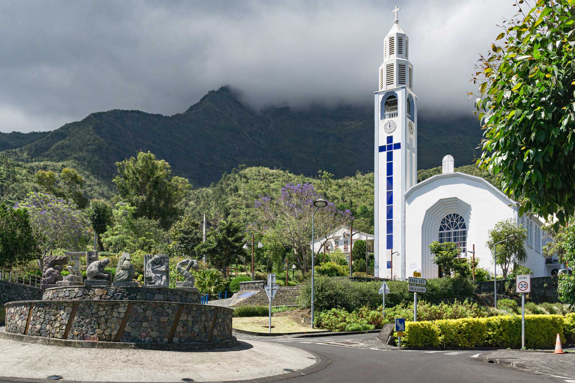 White Church with Blue Cross in Tropical Mountain Valley A modern white church with a tall bell tower featuring a prominent blue cross stands in a lush