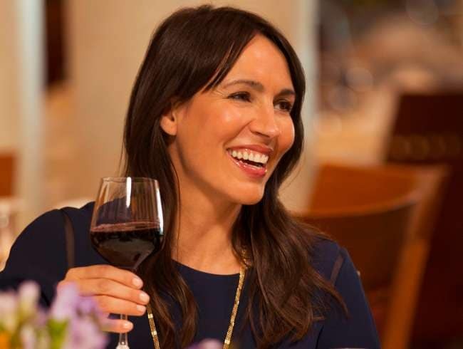Woman Enjoying Wine in Fine Dining A woman smiles while holding a glass of red wine in an elegant dining room with warm lighting