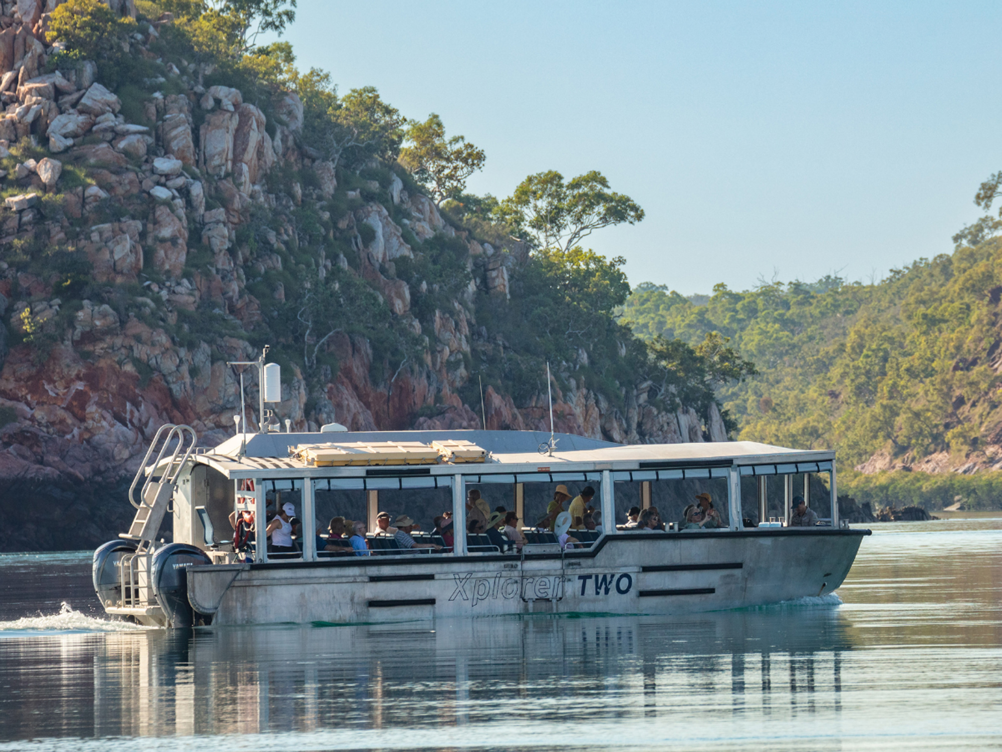 A scenic river cruise vessel named Xplorer Two navigates through a pristine waterway flanked